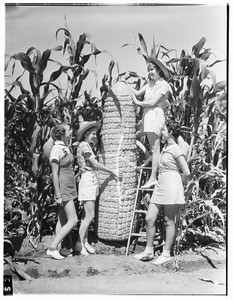 Four young women standing next to a giant ear of corn, Pomona County Fair, 1936