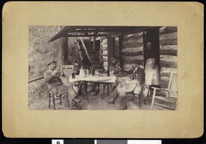 A group of fishing club members drinking liquor or wine, at a dinner table, outside a mountain residence, ca.1910-1920