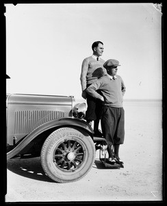 Two golfers standing on the front bumper of an automobile