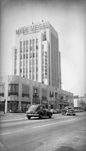 View of the 5400 block of Wilshire Boulevard showing a tall building and several automobiles, ca.1950-1959