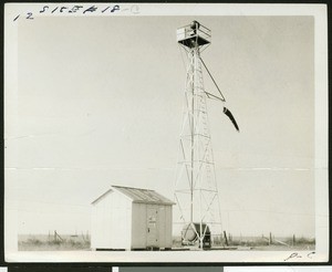 Windsock hanging from the right of the end of a metal tower on an unidentified airport, ca.1927