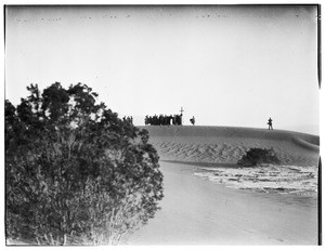 Group of people congregating around a cross in the distance at a funeral in the desert