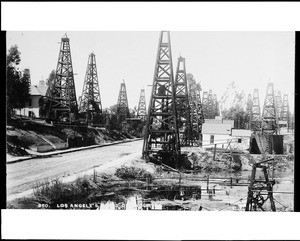Cluster of oil wells in Los Angeles, showing paved road at left, ca.1910