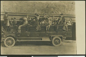 Open-air motor bus with people sitting and standing on top, ca.1900