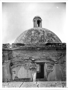 Indian Sacristan standing beside the dome of Mission Tumacacori, Arizona, ca.1908