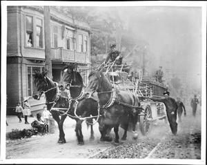 Early fire engine pulled by large muscular horses, up a hill on First Street, ca.1900