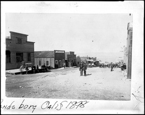 Building-lined dirt street full of people in Randsburg, 1898