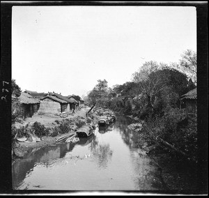 View along a still canal, littered with anchored skiffs in China, ca.1900