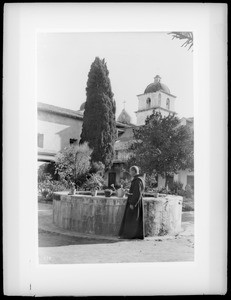 Father Superior Peter Wallischeck (Wallacecheck?) standing at outdoor fountain at Mission Santa Barbara, ca.1898