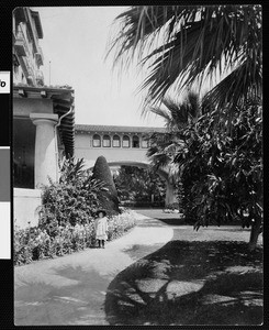 Young girl standing on the grounds of the Green Hotel with part of the bridge to its annex in view, ca.1905