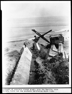 Construction of beach groins, showing a backhoe installing concrete blocks at the site of a new groin along the Southern California coast, 1953