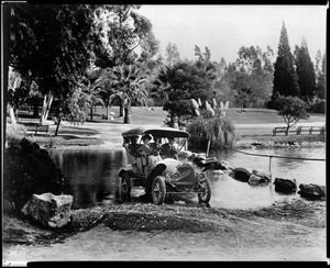 View of a 1908 "Tourist" automobile driving through a stream in Eastlake Park (later Lincoln Park), ca.1908