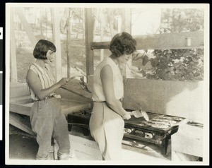 Women frying fish in a campground cooking area, ca.1930
