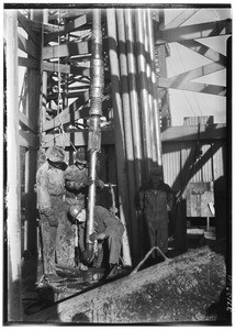 Four men adjusting a drill inside an oil well
