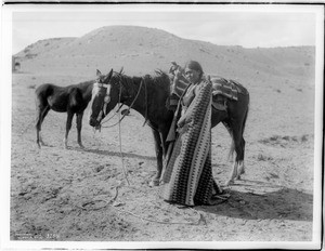 Navajo Indian maiden standing beside her pony, ca.1901