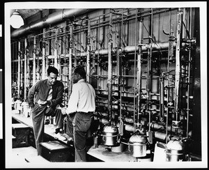 Shell Oil Company employees at work, showing two men standing in front of machinery, ca.1940