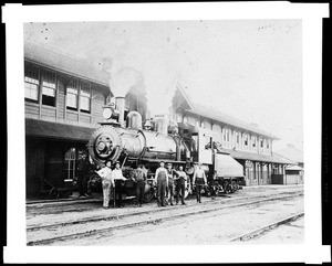 Men standing near a steam engine in front of the Harvey House in Mojave