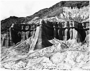 View of Red Rock Canyon with a man standing at the foot of cliffs, Death Valley, California, ca.1900/1950