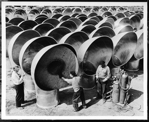 Workers inspecting rows of metal air vents for installation on ships in San Pedro