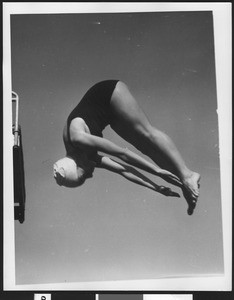 Female diver reaching for her toes as she dives, ca.1930