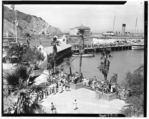 Hundreds of people lined up along the beach and on the pier of Avalon, showing a long line of people, Catalina Island