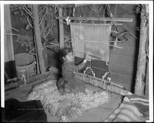 Portrait of a young Navajo Indian girl weaving a blanket, ca.1900