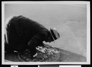 Frederic A. Batty, the Department of Public Works Superintendent of Sewers, crouching over a manhole to check for gas odor