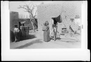 Woman carrying large pottery jar on shoulder and boy carrying two pails near small house, Juarez, Mexico, ca.1905