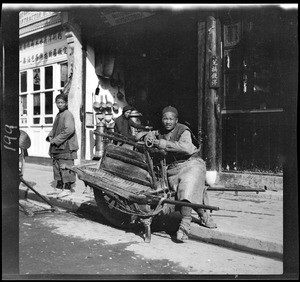 Portrait of a wheelbarrow taxi driver and his cart, China, ca.1900