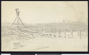 Two men looking down upon wooden planks across a small stream, ca.1910