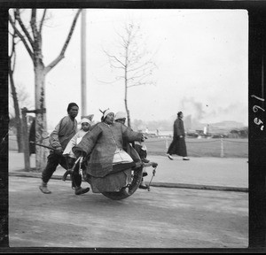 Family of three being conveyed in a wheelbarrow taxi in China, ca.1900