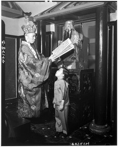 Buddhist priest and child in front of a religious statue (?), showing the young girl speaking, Chinatown