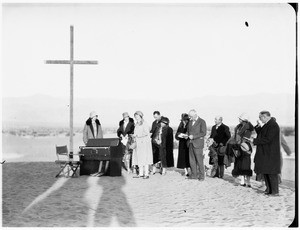 People gathered around a cross for a funeral in the desert