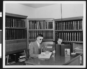 J. Robert Atkinson at a desk reading from a book for the blind, in December 1933