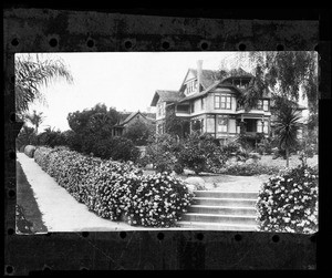 Exterior view of a residence in Santa Barbara, showing rose bushes and Queen Anne home, ca.1900