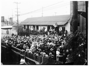 Large crowd during Mexican Independence (day?), gathered against a long ranch house