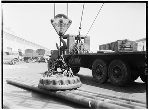 Steel pipe being loaded onto a flatbed truck via a large magnet at Los Angeles Harbor, 1930