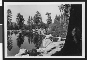 Two women and a man seated on rocks overlooking Bartlett's Cedar Lake near Big Bear Lake, ca.1950