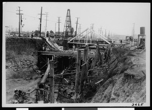 Construction taking place below an unidentified wooden bridge