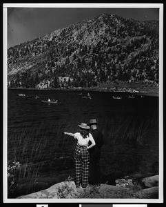 Man and a woman standing at June Lake, showing boats on the water, ca.1950