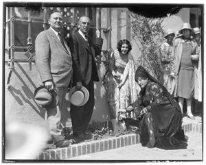 Two women in Spanish dress pushing a shovel into the ground next to two men