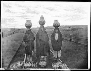 Three Pueblo Indian women displaying their ollas for sale at the railroad tracks, New Mexico, ca.1900