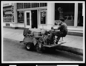 Department of Public Works employee driving equipment along the curb of a commercial street