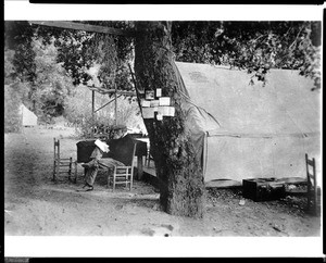 Sunset Club member J. M. Elliot reading in front of his tent, ca.1900