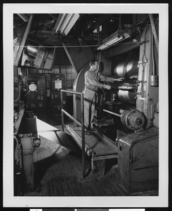 Factory worker working with large machinery, ca.1950