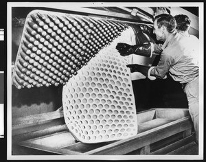 Man stripping a piece of completed c-foam from a mold at the American Latex Products Corporation, ca.1950