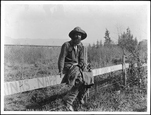Hobo sitting on a fence, ca.1920