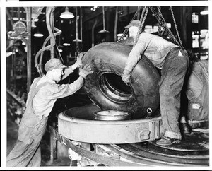 Two workers pulling a rubber tire from its mold at an unidentified factory in California Heights, 1930-1940