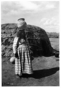 Pregnant(?) Pima Indian woman carrying an olla (water jar) on her head, Gila River Reservation, ca.1900