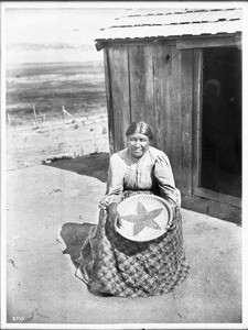 Ramona Lubo, wife of Alesandro, at her home, showing the star basket she made in his memory, ca.1905